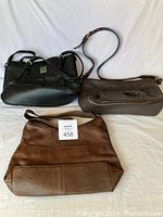 Three leather handbags arranged on white fabric backdrop showing front, side and top views.