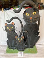 Full frontal image of the black cat sculpture showing all three cats on a green base with the clamp visible supporting the tail of the largest cat.