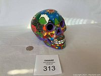 Side view of the colorful hand painted ceramic skull on a flat surface with a quarter for scale.