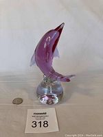 Full view of purple glass dolphin figurine on clear base with quarter for scale.