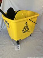 Side view of yellow Rubbermaid mop bucket with mounted wringer, showing caution symbol and caster wheels.