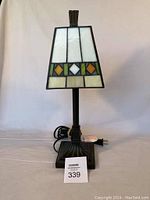 Front view of Tiffany style desk lamp showing stained glass shade with geometric pattern and metal base with power cord.