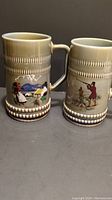 Two vintage Irish porcelain tall beer tankards with distinct painted scenes and detailed handles.
