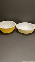 Two yellow Pyrex bowls side by side showing size difference and shape.