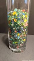 Clear glass container filled with assorted colorful vintage marbles, showing full amount and colors in detail.
