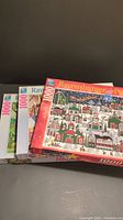 Photo showing three Ravensburger 1000 piece puzzle boxes stacked, featuring colorful illustrated scenes on the packaging.