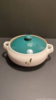 Full view of the white ceramic casserole dish with teal lid and green wheat decoration.