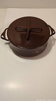 Top view of brown enameled casserole with lid showing cross-shaped handle design and side handles.
