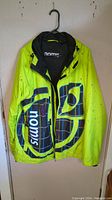 Front view of the bright yellow Nomis ski jacket showing large logo and front zipper.