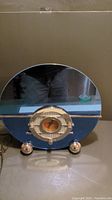Full front view of Thomas Museum Series radio showing reflective glass front, circular gold-tone tuning dial with three knobs, and spherical feet.