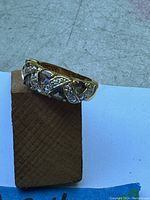 Front view of a 10K gold ladies ring with an intertwined pattern of translucent and small clear stones on top.