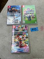 Photo shows three Nintendo Switch game cases on a table: Immortals Fenyx Rising, LEGO DC Villains, Mario Kart 8 Deluxe. A small sticky note with '#39' is placed near the cases.