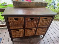 Front view of the wooden storage cabinet showing six woven basket drawers in two rows of three, standing on a wooden floor.