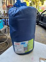 Sleeping bag compressed in blue sack, showing label with brand, model, and comfort range.