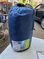 Photo of the Coleman sleeping bag compressed in navy blue stuff sack on a table outside.