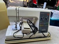 Side view of Kenmore 22 sewing machine showing foot pedal, power cord, and cream plastic body on table outdoors.