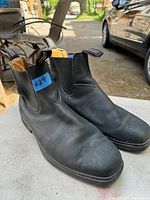 Pair of black leather Blundstone boots, showing front and side views on a table outdoors.