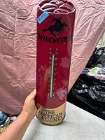 Full view of the metal Winchester thermometer showing the cowboy rider logo, temperature scale, and slogan at the bottom.