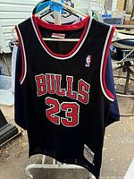 Black Chicago Bulls basketball jersey with Michael Jordan #23 on front and back, hanging on rack outdoors.
