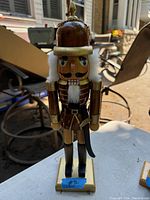 Front view of the solid wood nutcracker figurine showing detailed painted features, white hair, and sword accessory attached to the belt.