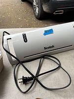 White Scotch laminator with power cord neatly coiled on a table, showing the control buttons and branding clearly.
