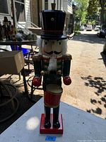 Front view photo of tall wooden nutcracker standing on a table outdoors with visible details of paint and facial features.