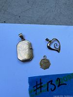Photo of three 10K gold pendants placed on white background showing front of rectangular locket, heart pendant, and small round medallion.