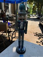 Full view of wooden nutcracker figurine standing on tabletop outdoors, showing front and side details.