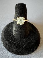Front view of 10k gold ring with synthetic center stone mounted on black display stand.