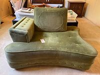 Front view of the green velour chair showing the wide curved seat, button tufting and one armrest.
