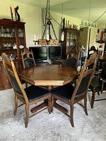 Full view of the octagonal wooden dining table with four side chairs showing the table's shape and the chairs' black padded seats and backs with carved wooden frames.
