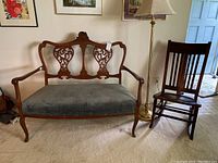 Antique wooden settee, rocking chair, and brass floor lamp positioned together in a living room area, showing carved details and upholstery.