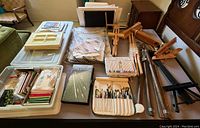 Overview of multiple wooden easels, paintbrushes, colored pencils, paint palettes, papers and art supplies arranged on bed