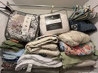 Stacked bedding on metal rack with plastic and metal hangers showing comforters, blankets, and folded bedding.