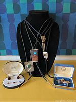Five bolo tie slides on braided cords displayed on a black bust