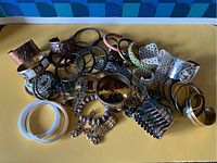 Large assortment of bracelets and cuffs laid out on yellow surface showing variety of materials and styles.