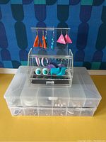 Clear view of six pairs of colorful costume earrings displayed on an acrylic earring stand with multiple transparent storage boxes below