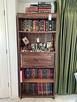 Full bookcase displaying leather-bound volumes on three shelves, top shelf with loose stack of additional volumes