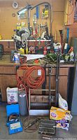 Overall view of workbench and pegboard with various tools, extension cords, chemicals, clamps, and other supplies arranged in a garage.