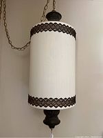 Front view of hanging swag lamp showing white cylindrical textured shade with dark decorative trim and dark metal fixture with chain