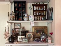 Wide view showing a shelf with assorted miniature ceramic and pottery vases, framed paintings, glass marbles, and other decorative items