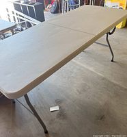Full view of beige plastic folding table set up with foldable metal legs.