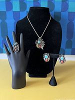 Full view of pendant on display bust, ring on stand, earrings on stand