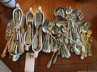 Photo showing a large quantity of assorted stainless steel flatware including forks, spoons, serving spoons, and a set of gold-tone small spoons