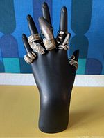 Front left side view of the seven sterling silver rings displayed on a black hand mannequin showing tarnish and design details.