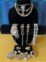 Front view of jewelry displayed on black jewelry stand including two necklaces, four bracelets and several pins and earrings laid at the base.