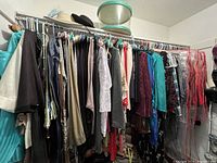 Wide view of women's clothes on hangers in closet, showing a dense assortment of garments mostly in dark and neutral colors with some bright pieces.
