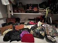 Wide shot showing the entire collection of various women's purses laid out on the floor and a shelf above filled with additional bags and purses.