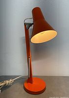 Front view of the orange desk lamp lit, showing shade and base.