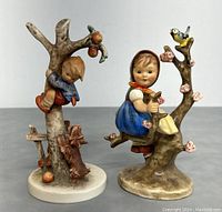 Front view of two Hummel figurines, one boy climbing tree with dog, other girl sitting on tree branch with bird